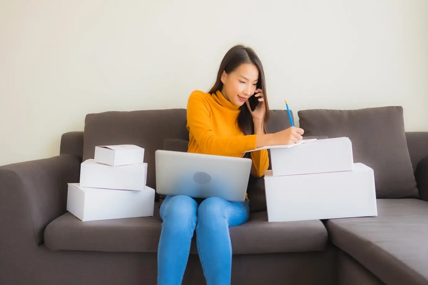 Portrait of a young Asian woman working on a laptop with a parcel box.