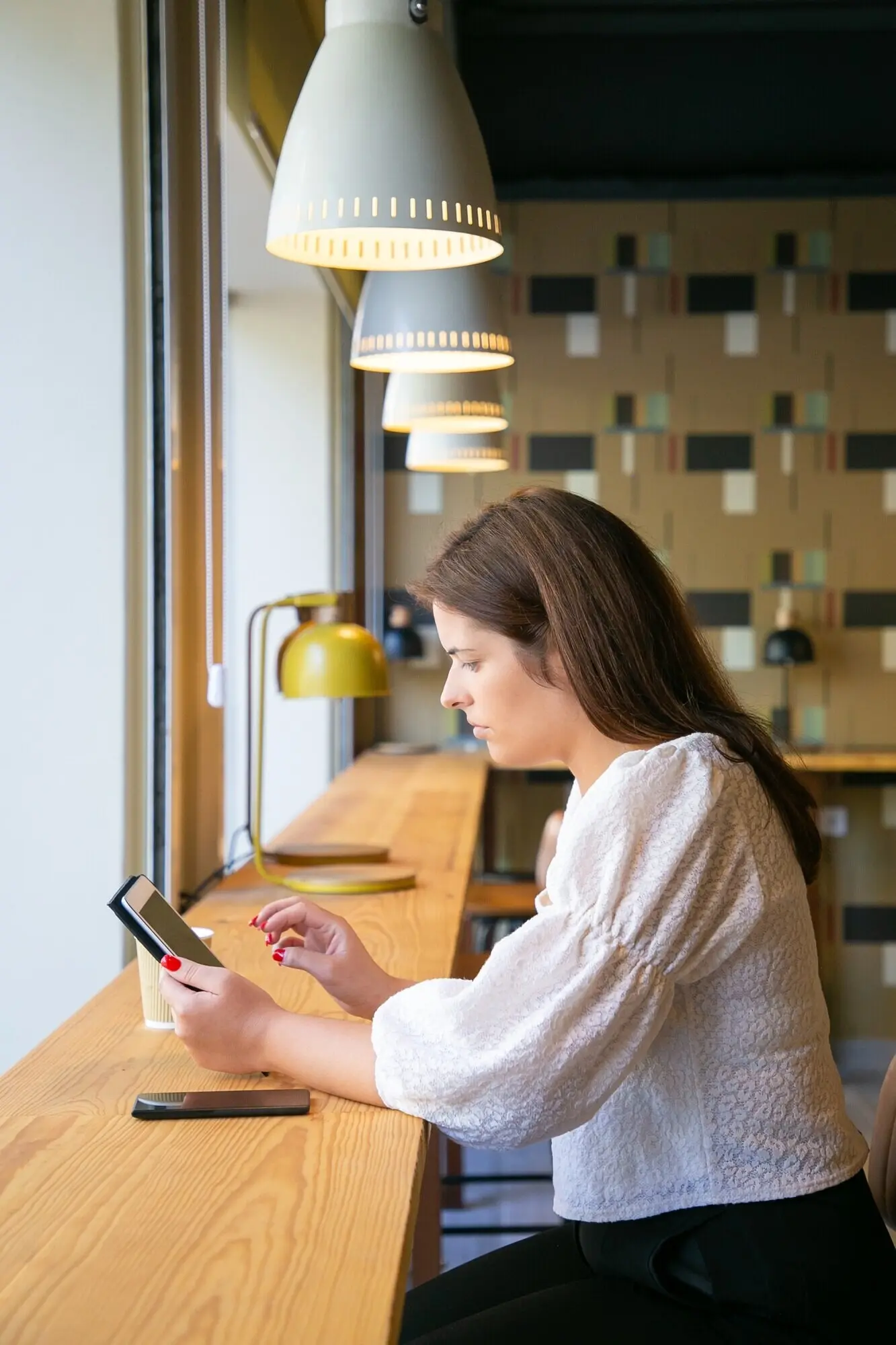 A focused female manager uses a tablet while seated at a desk in a co-working space or coffee shop.