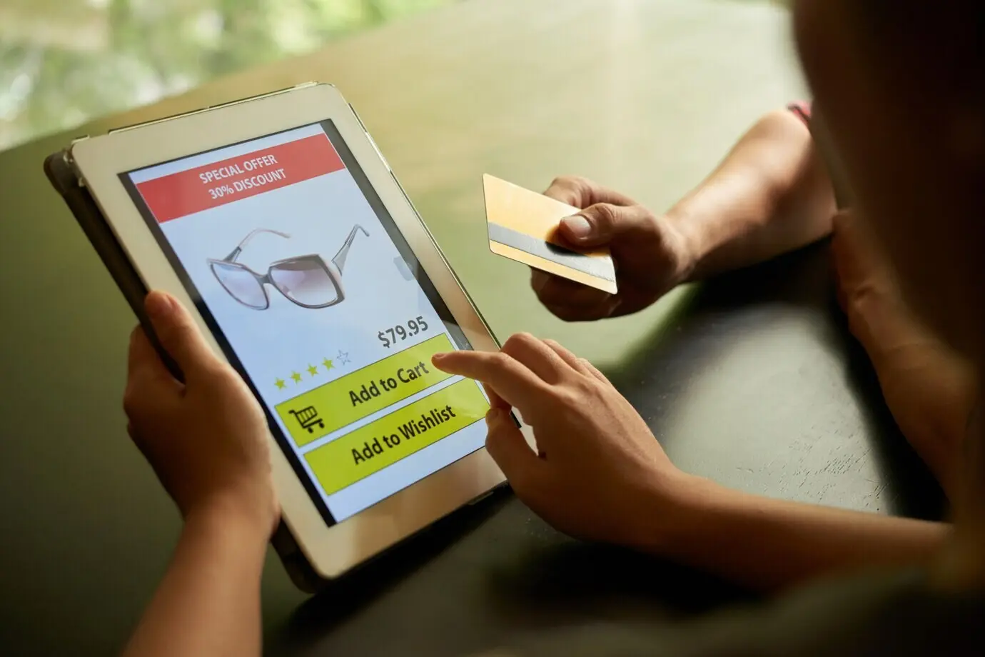 Concept of online shopping featuring two unrecognizable people adding sunglasses to a cart on a tablet PC.